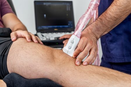 Close-up of a physiotherapist performing an ultrasound of the knee on a patient lying on the stretcher
